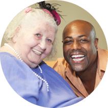 a smiling elderly female with a smiling male caregiver